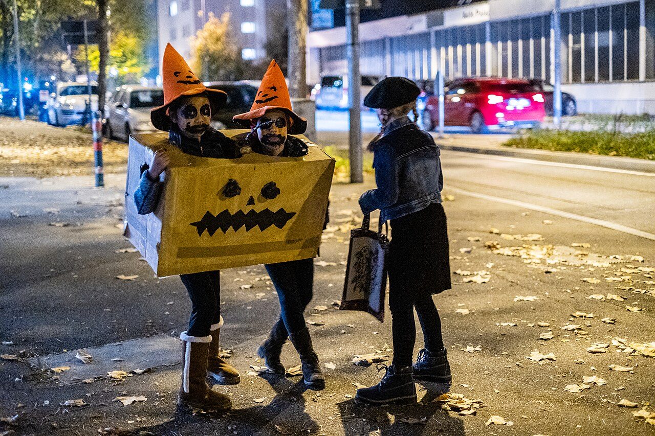 Bambini con costumi di Halloween fai da te: una scatola di cartone dipinta a zucca, cappelli arancioni e trucco sul viso