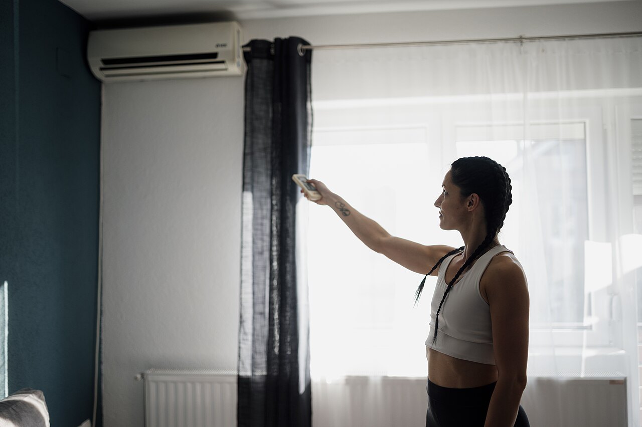 Una donna regola con il telecomando il climatizzatore a parete in un soggiorno moderno, con il termosifone sotto la finestra