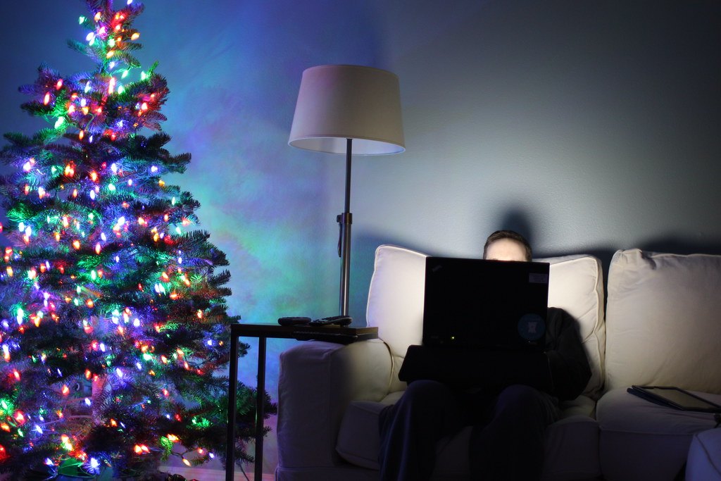 Una persona sul divano con il portatile acceso accanto a un albero di Natale illuminato