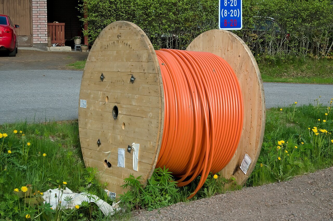 Una bobina di legno con il cavo arancione della fibra ottica, appoggiata sul ciglio di una strada prima della posa