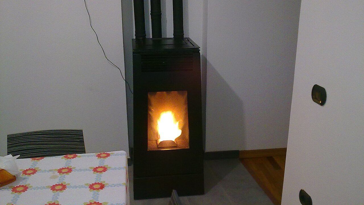 Stufa a pellet nera accesa in un soggiorno, con la fiamma nel braciere e i tubi dei fumi a parete
