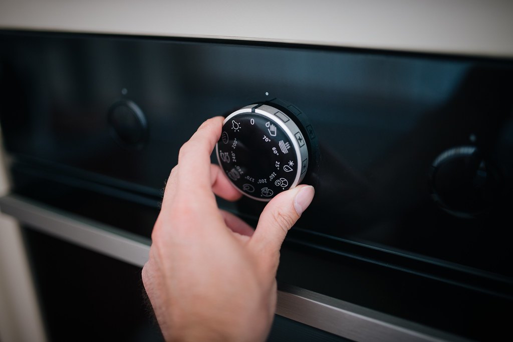 Una mano regola la manopola della temperatura di un forno elettrico da incasso nero