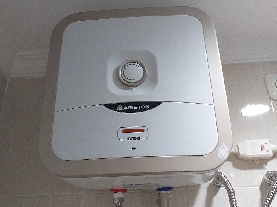 Uno scaldabagno elettrico Ariston montato a parete in bagno, con i tubi flessibili dell'acqua calda e fredda