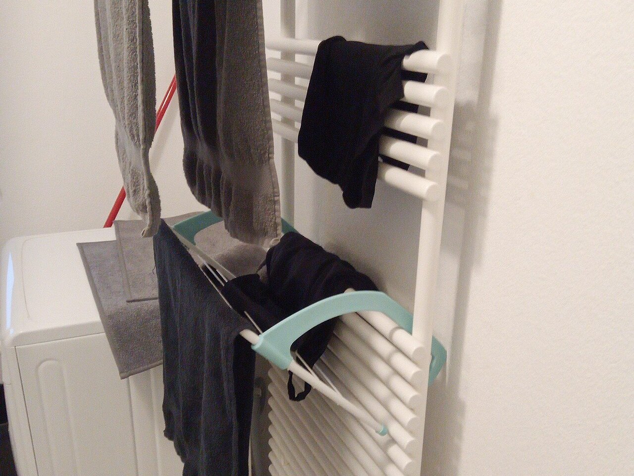 Uno stendino pieghevole agganciato a un termosifone da bagno, con asciugamani e panni stesi ad asciugare