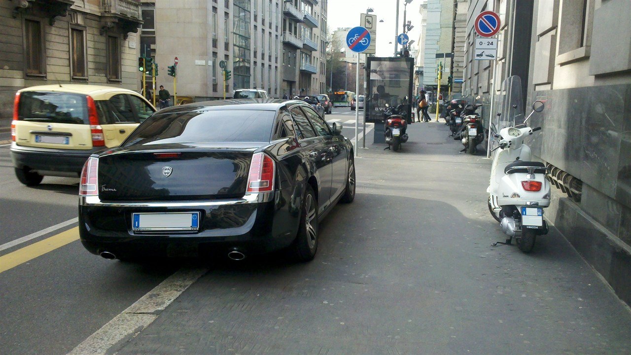 Una berlina nera e una Vespa bianca ferme in una via del centro di Milano