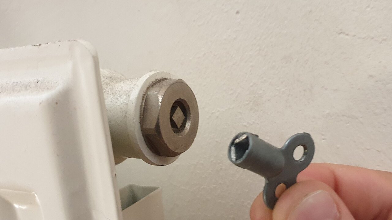 Mano che infila la chiave di sfiato nella valvola in alto a un termosifone