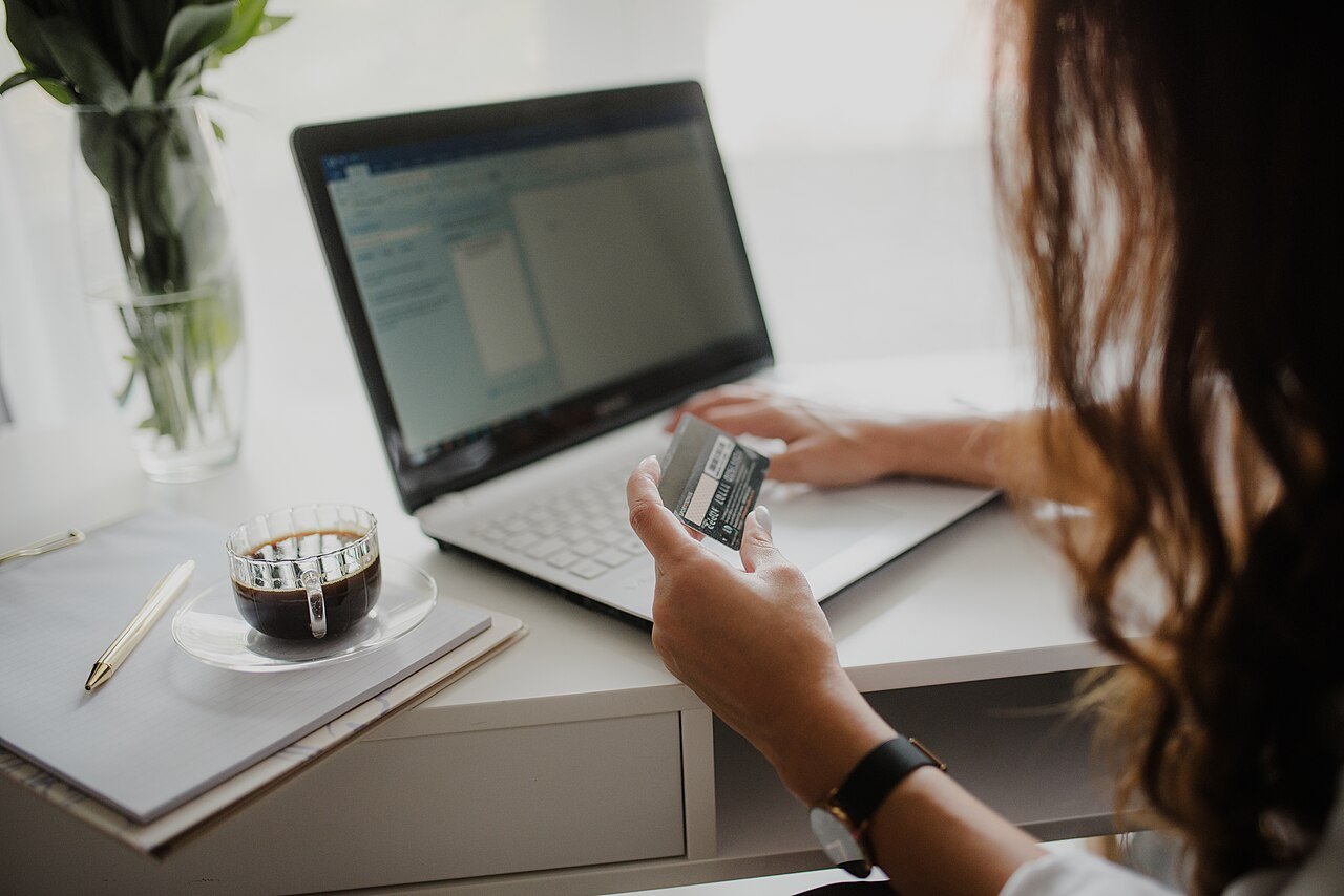 Donna con una carta di pagamento in mano davanti al portatile mentre fa un acquisto online