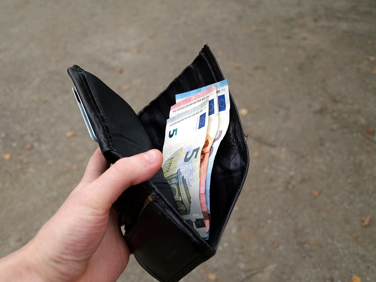 Un portafoglio nero aperto in mano, con tre banconote da 5, 10 e 20 euro