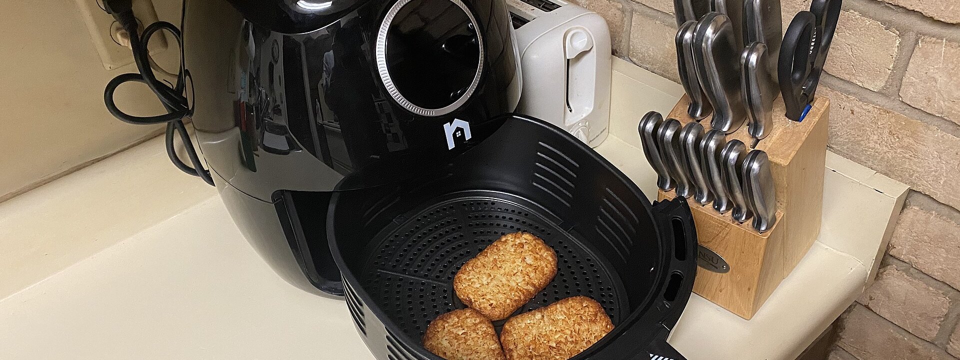 Friggitrice ad aria nera con il cestello aperto sul piano della cucina