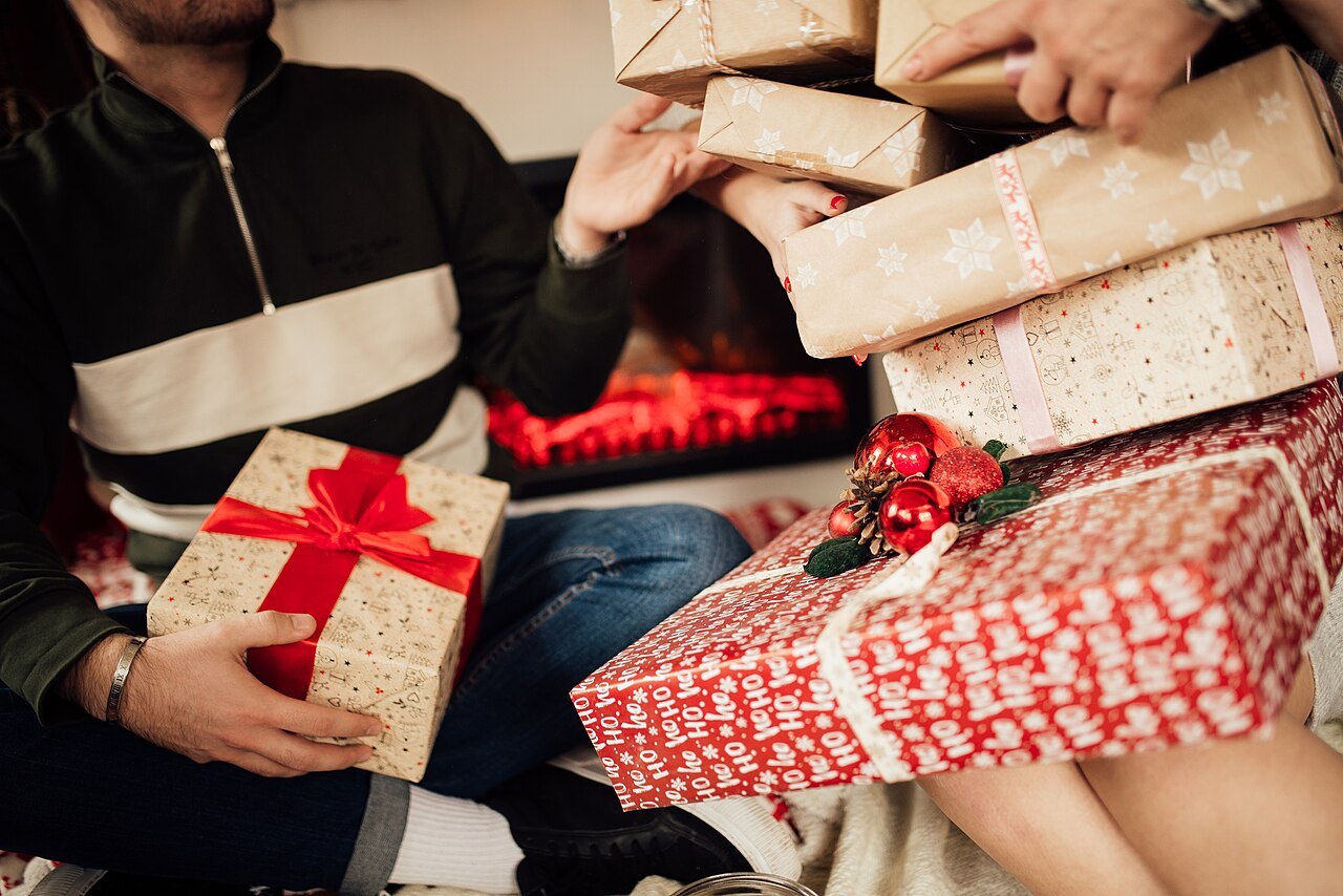 Una coppia seduta davanti al camino si scambia pacchi regalo di Natale incartati con fiocchi rossi