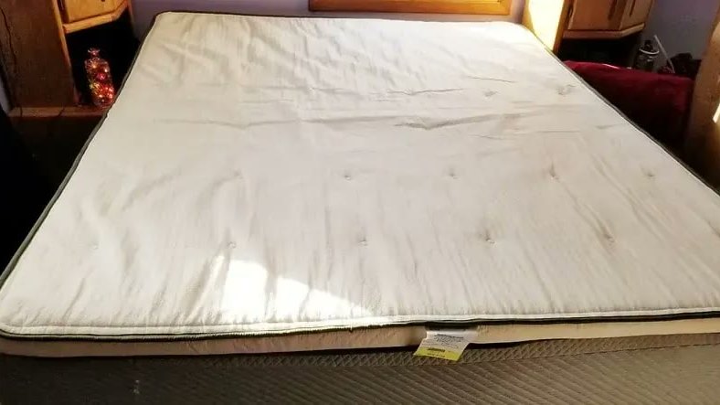 Topper imbottito bianco steso sopra un materasso matrimoniale