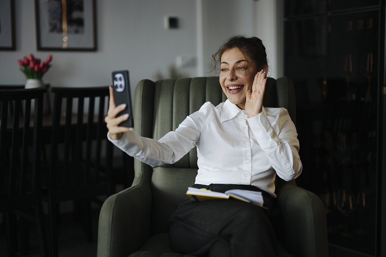 Donna seduta in poltrona che saluta in una videochat dal telefono