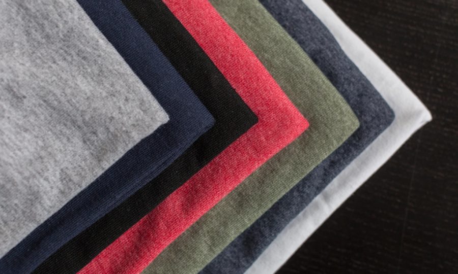 Magliette di cotone di più colori piegate una sopra l'altra, su un piano scuro